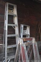 Two aluminum ladders, one 6 ft and one 4 ft tall, leaning against a wall with two wooden sawhorses in front of them.