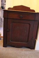 Front view of wood cabinet with a single drawer above a cupboard door. Cabinet finish is visibly worn.