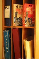 Books and binders on shelf including two Harris Catalogs of postage stamp prices, a blue Canada stamp album, and a red binder.