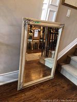 Full view of rectangular mirror with beveled glass and decorative wood frame resting against wall near hardwood stairs