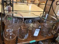 Multiple clear glass bowls, vases, plates and a metal bell arranged on a wooden shelf