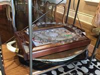 Stack of trays including a wooden tray with embroidered fabric, a clear glass plate with decorative round edge beads, a metal tray and a plastic tray underneath.