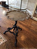 Full view of the decorative metal top table with scalloped edges and twisted black metal legs on wooden floor