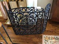 Front angled view of cast metal fireplace screen showing ornate scroll and floral design.