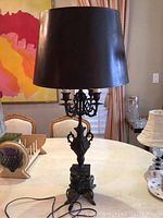 Full view of the vintage metal candelabra lamp with dark lampshade on a table, showing overall shape and design.