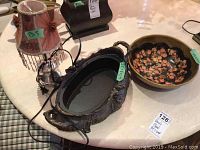 Image of metal teapot-shaped lamp with pink fabric shade, metal holder tray, and painted wood floral bowl on a marble table.