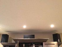 Three speakers (left bookshelf, center channel, right bookshelf) on shelf under recessed lights