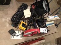 Photo of assorted electronics including black Sanyo M7022 stereo, charger, cables, and a red item on concrete floor