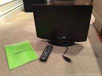 Insignia 19 inch LCD TV, remote control, and green user manual on a beige carpet