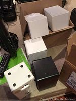 Speakers including white and black units shown in a group with some speakers on a box.