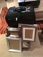 Swissgear suitcase with four assorted picture frames arranged on the floor in front of it.