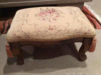 Front view of needlework upholstered stool showing floral design and carved wood legs with tassels.