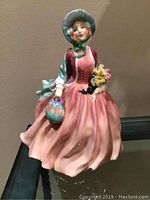 Front view of Royal Doulton figurine, showing woman in pink dress holding flowers and purse.