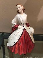 Front and left side view of the Royal Doulton 'The Ermine Coat' HN1981 figurine showing the woman in a white ermine coat over a red dress with red gloves.
