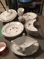 Full view of the porcelain serving dishes and tea set, showing serving bowl with lid, bowls, demilune dishes, teacups, demitasses, and plates featuring floral patterns and gold trim.