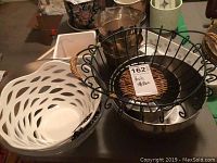 Wide view of wire basket on top of a silver bowl and white cutout plastic bowl to the left with other items in the background