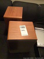 Front and rear views of two wood veneer cube speakers on a couch