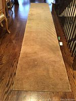 Full view of beige runner rug laid on wood floor next to staircase and chairs.