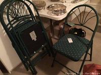 Four green metal folding chairs stacked together, showing the seat upholstery and back design.