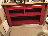 Front view of red Stack-On metal work bench showing two drawers, two open storage compartments above the shelf, and a large bottom shelf.
