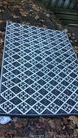 Full view of the outdoor patio carpet laid out on wooden deck with leaves around. Shows black and white geometric diamond pattern.