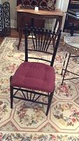 Front view of black painted wooden chair with red cushion, showing spindled backrest and wear on paint.