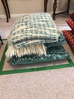 Stack of the Urban Barn throw blanket on top of two teal textured looped pillows arranged one on top of the other on carpet.