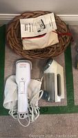 Photo showing three items: a Sunbeam travel iron with cord, a garment steamer with pouch and manual, and a battery-operated clothes shaver without power cord.