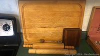 Image showing a large light wood cutting board with grooved edges, two smaller dark wood cutting boards, and two wooden rolling pins placed on a countertop.