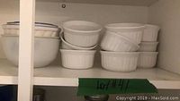 Shelf with stacked white ceramic ramekins, including 10 smaller and 4 larger pieces, in a cupboard