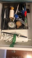 Drawer containing knives, a meat thermometer, twine, kitchen scissors, and a white handheld electric mixer.