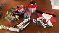 Photo showing the assortment of baking supplies including hand blender, vintage electric whisk with attachments, mixing bowls with red lids, measuring spoons, dough scraper, pastry brush, rolling pin, knife sharpener and other baking tools laid out on a wooden surface.