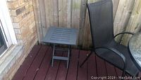 Small gray side table next to a black mesh chair on a wooden deck
