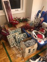 Photo showing boxes of large blue and silver ornaments next to decorative greenery and some bins with assorted Christmas decorations