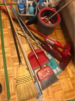 Various cleaning tools including mops, brooms, vacuum sticks, dustpan and cleaning supply caddies.