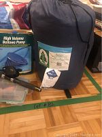 Two rolled sleeping bags in dark blue storage sacks along with a blue pneumatic (bellows) pump box and a black fishing rod handle.