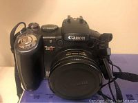 Front view of Canon PowerShot S5 IS camera with lens cap and strap attached.