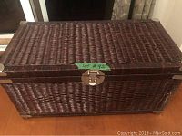 Front view of the dark brown wicker storage box with closed lid and metal locking clasp.