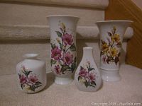 Four Kaiser porcelain floral vases arranged on steps, showing pink 'Liliane' and yellow 'Arlette' patterns.