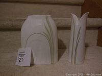 Front view of two white Royal Daulton ceramic pieces: a medium Cypress vase with a soft rectangular rounded shape and a flared top, alongside a Petal candle stick with petal-like flared opening. Both have green linear stripe design.