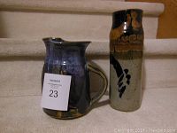 Handmade blue pottery pitcher and decorated pottery vase on carpeted stairs.