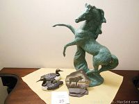 Photo showing large ceramic horse statue in rearing position, ceramic loon pair, and ceramic moose plaque arranged on table.