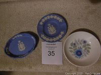 Top view of two Wedgwood pin dishes, one blue with Coat of Arms Canada and one white with floral pattern, displayed on carpet.