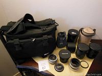 Full view of camera equipment lot including the black fabric camera bag, multiple lenses with caps, lens holders, and pouches arranged on a wooden surface.