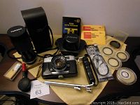 Full view of the vintage Konica camera, Tamron lens with case, camera holder attachment, Kodak lens cleaning kit, multiple lens filters and cleaning accessories laid out on a table.