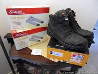 Lot contents showing the pair of black STC work boots sized 11, displayed on top of the orange and white STC box with Made in Canada label, alongside two boxed Sunbeam shoe ionizers in original packaging.