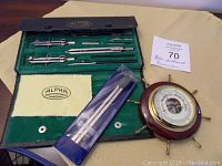 Full view of Alpha Precision Instruments case with drawing tools and separate barometer on a beige cloth.