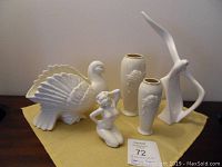 All items displayed together on a yellow fabric: two cream Lenox vases, ceramic pigeon, seagull, and nude female figurine.