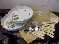 Full view of two rose motif quiche plates, cream-handled cutlery set, and glass cheese dome on yellow cloth.