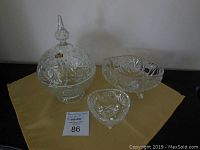 Three crystal bowls displayed on yellow cloth; includes round lidded bowl, oval bowl, and triangular bowl.